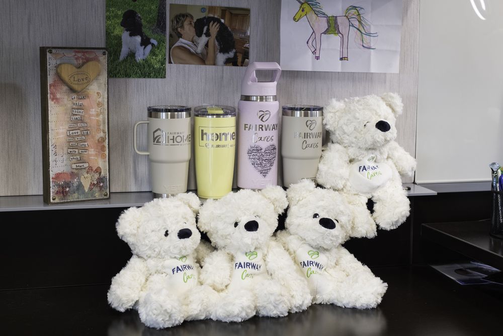 Fairway Cares teddy bears and tumblers arranged on a desk beside children's drawings